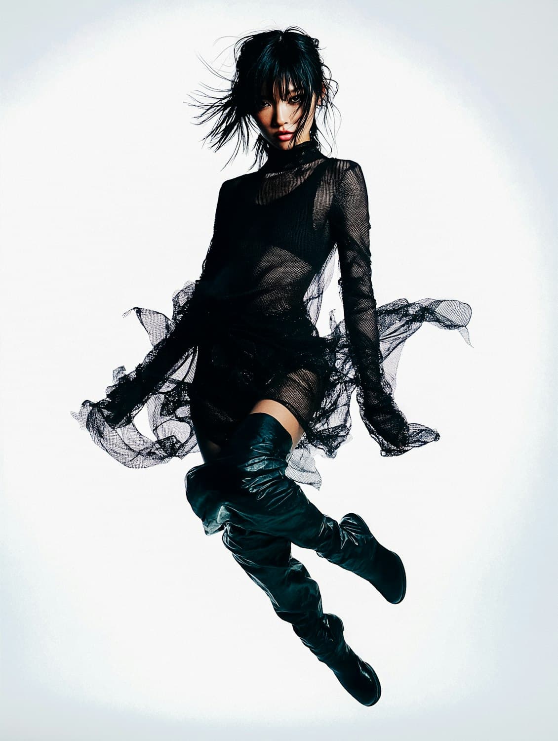 Model leaping mid air in a sheer black dress and thigh high leather boots.