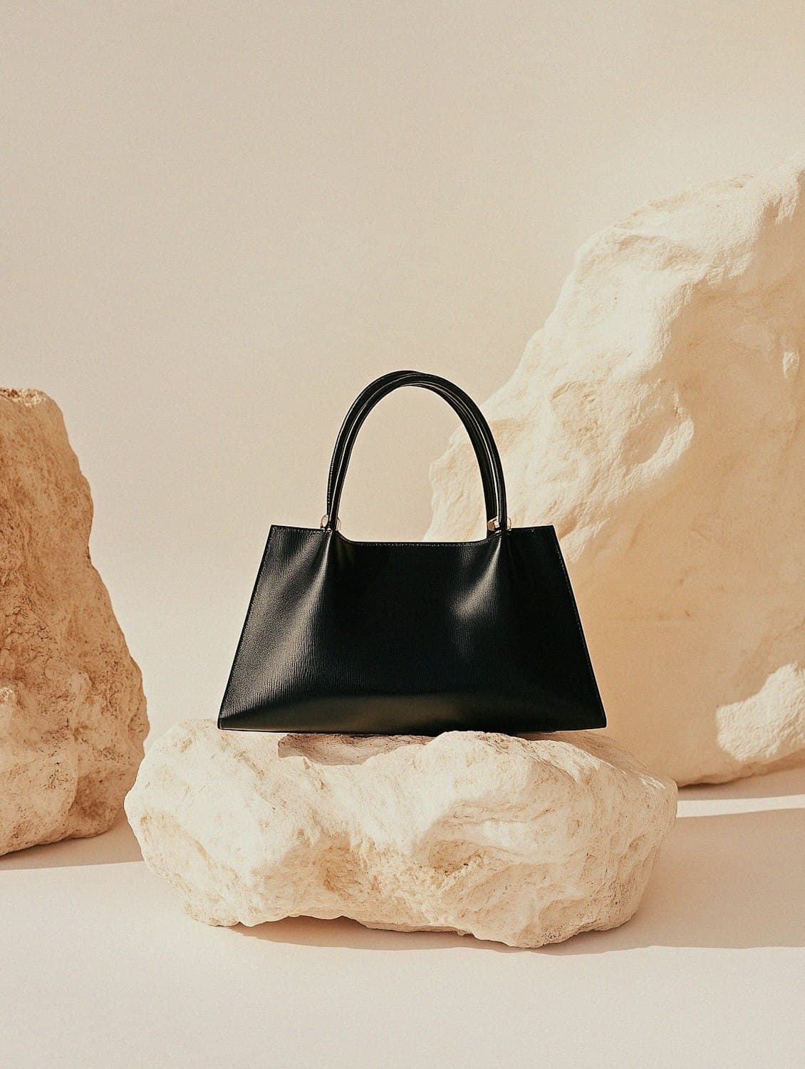Structured black leather handbag resting on a pale limestone rock in warm afternoon light.